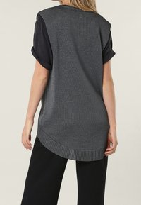 Haut en tricot gris texturé avec une coupe décontractée, manches courtes retroussées et ourlet arrondi. Associé à un pantalon noir à jambes larges.