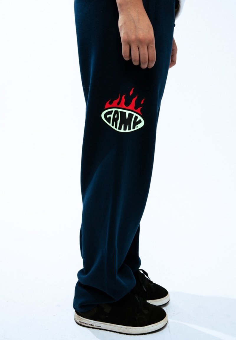 Granatowe dresy o luźnym kroju z dużym zielono-czerwonym logo płomienia i napisem "GRMC" na lewym udzie. Czarne sneakersy.
