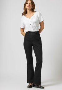 Pantalones de campana negros combinados con una blusa blanca de mangas cortas que presenta pliegues y un escote con botones. Zapatos planos completan el conjunto.