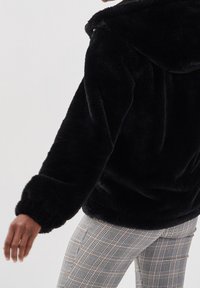 Sort faux fur hoodie med afslappet pasform, der har en hætte og elastiske manchetter, parret med grå ternede bukser.