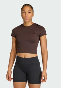 Καφέ κομμένη αθλητική μπλούζα και μαύρο σορτς με ψηλή μέση, και τα δύο από λείο, ελαστικό ύφασμα. Διακριτικό λογότυπο στο στήθος και στον μηρό.