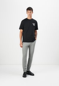 Svart bomulls t-skjorte med grafikk på forsiden, kombinert med grå elastiske treningsbukser og svarte sko. Enkelt design, tettsittende snitt, minimal stil.