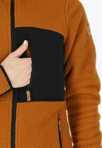 Giacca in pile con un corpo arancione testurizzato e accenti neri lisci. Presenta una tasca sul petto con zip e una vestibilità comoda.