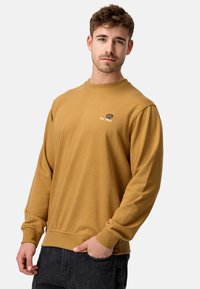 Sennepsgul sweatshirt med lange ærmer, ribbet halsudskæring og manchetter, samt broderet logo med "Est. 1993" på brystet.