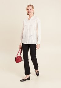White cotton shirt with eyelet embroidery, black fitted pants, black flats with strap detail, and a small red crossbody bag.