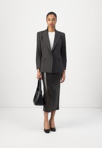 Blazer à double boutonnage à rayures en gris foncé sur un haut blanc, associé à une jupe midi en cuir noir ajustée et des chaussures à talons hauts noires.