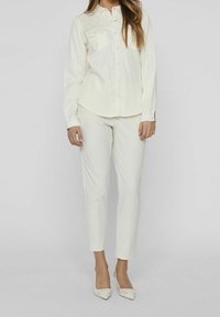 Chemise blanche à manches longues avec deux poches poitrine. Associée à un pantalon blanc slim et des talons assortis. Tissu lisse et coupe ajustée.