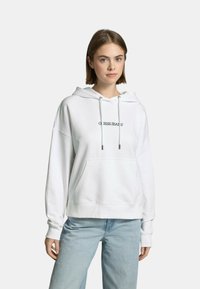 Felpa bianca in cotone con tasca frontale, vestibilità oversized, cappuccio con cordino e logo "Guess Jeans" in nero sul petto.