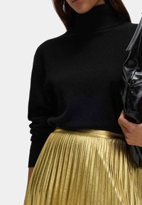 Sort strikket højhalset sweater kombineret med en skinnende gylden plisseret nederdel. Sættet har en glat tekstur og en slank sort taske.