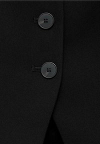 Černá tkanina s hladkým povrchem, která obsahuje dva kulaté knoflíky. Knoflíky jsou tmavé a lesklé, umístěné blízko zahnutého okraje materiálu.