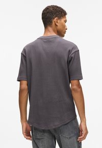 Anglies pilkos spalvos trumpomis rankovėmis marškinėliai su vaflinė tekstūra, apvaliu iškirpimu ir šiek tiek kreivu apačiu, parodyti derinami iš nugaros.