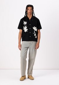 Zwarte T-shirt met korte mouwen met witte bloemenborduursels aan de linkerkant, gecombineerd met lichtblauwe jeans en beige sneakers.