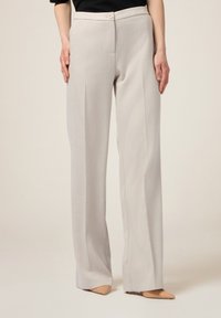 Lichtgrijze, wijde broek van textuurstof met een knoopsluiting en voorkruiden, gecombineerd met nude puntige schoenen.