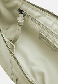 Interno di una borsa in pelle color beige chiaro con rivestimento in tessuto morbido, dotato di una tasca con zip e un'etichetta con logo. Design minimalista con cuciture sottili.