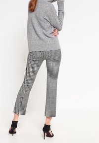 Gray knitted sweater with ribbed texture paired with black and white houndstooth patterned trousers, finished with black high-heeled shoes.