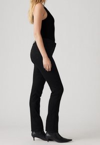 Jeans de mezclilla negra con corte recto, que presentan bolsillos traseros con detalles de costura, combinados con una blusa sin mangas negra y botas de tobillo negras.