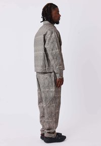 Chaqueta gris con un patrón y pantalones a juego en un tejido texturizado, que presentan un corte relajado y detalles de costura visibles. Un calzado negro completa el conjunto.