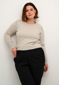 Striped long-sleeve top in beige and off-white, featuring a round neckline and ribbed cuffs, paired with black tailored trousers.