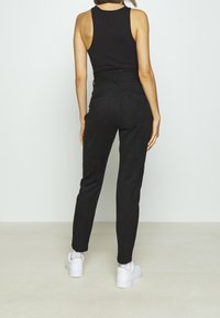 Svarta mocka byxor med hög midja, slim fit, avsmalnande ben och bakfickor, tillsammans med vita sneakers och en svart linne.