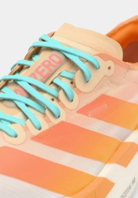 Close-up van een oranje en beige sneaker met lichtblauwe veters en het woord "ZERO" in rood op de tong.