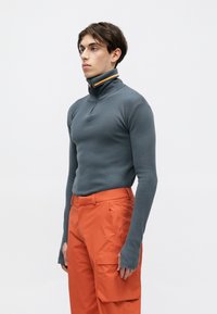 Grijze long sleeve pullover met een hoge kraag, voorzien van een multi-gelokt gestreept accent en een getailleerd ontwerp, gecombineerd met oranje cargobroek.