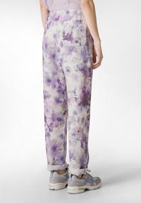 Losse, lichte linnen broeken met een lichtpaarse bloemenprint, voorzien van een elastische tailleband en een achterzak. Opgerolde boorden zichtbaar.