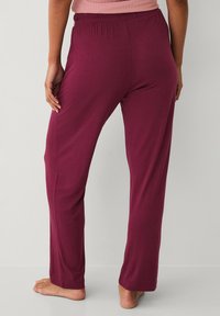 Burgundy lounge pants with an elastic waistband, soft fabric, straight leg design, and a smooth texture. No additional patterns or hardware visible.