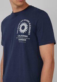 Navyblaues Baumwoll-T-Shirt mit Rundhalsausschnitt, das ein weißes Grafikdesign einer Blume und darüber liegenden Text zeigt. Kurzärmelig und mit lockerer Passform.