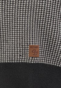 Sweter dzianinowy w wzór houndstooth w czerni i szarości. Posiada ribbowy, ciemnoszary ściągacz oraz brązową skórzaną metkę z logo.