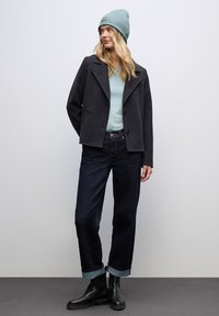 Tmavě šedý saka, světle modrá košile, tmavě modré džíny s ohrnutými nohavicemi, černé kotníkové boty a tyrkysová pletená čepice. Jednoduchý design.