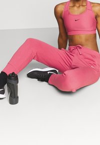 Rosa Nike Sport-BH und passende Jogginghose, aus weichem Material mit verstellbarem Kordelzug. Schwarze Wasserflasche und Schuhe mit weißen Akzenten.