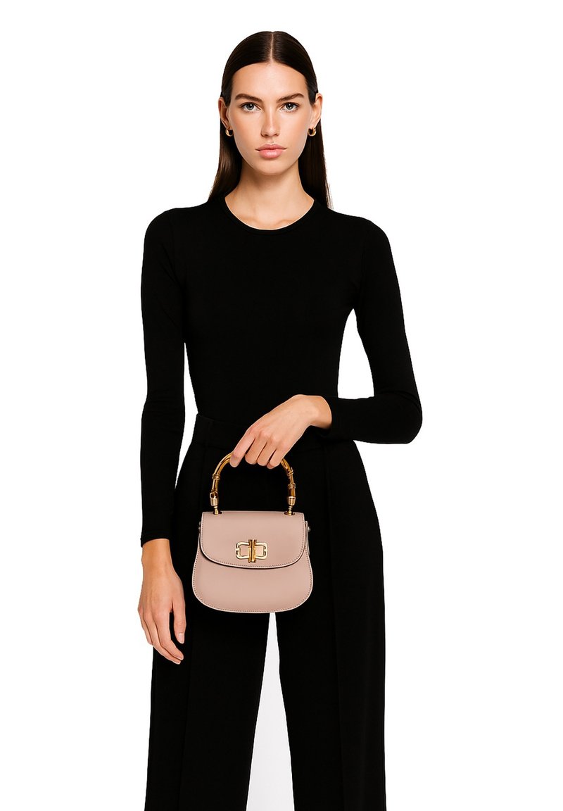 Kleine lichtroze handtas met een gestructureerde vorm, gouden hardware en een handvat in bamboestijl. Het model draagt een zwart lange mouwen jurk.