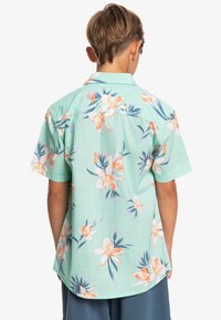 Kurze Ärmel, mintgrünes Shirt mit floralem Druck in Pfirsich und Blau. Leichte Stoffqualität mit lockerer Passform und abgerundetem Saum.