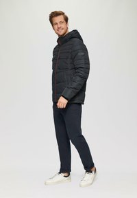 Zwarte pufferjack met capuchon, rits aan de voorkant, rode accenten en borstzakken. Gemaakt in combinatie met donkere broek en witte sneakers. Glad textuur.