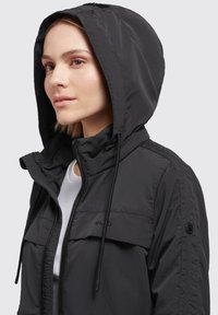 Black hooded jacket featuring a zip front, drawstrings, and shoulder epaulets. Made from lightweight material with a smooth texture.
