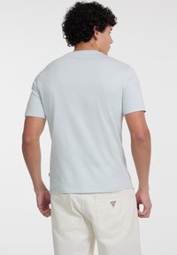 Gaiši zila īsām piedurknēm T-krekls ar apaļu kakla izgriezumu, izgatavots no mīkstas kokvilnas, valkāts kopā ar baltām biksēm ar nelielu logotipa detaļu.