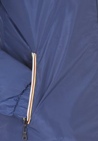 Primo piano di una manica di giacca blu navy con polsino elasticizzato e zip chiusa che presenta un trim a strisce rosse, gialle e nere.