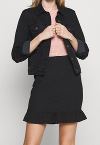 Svart denimjacka med knappstängning och två bröstfickor, i kombination med en rosa rutig topp och en figurformad svart kjol med volangkant.