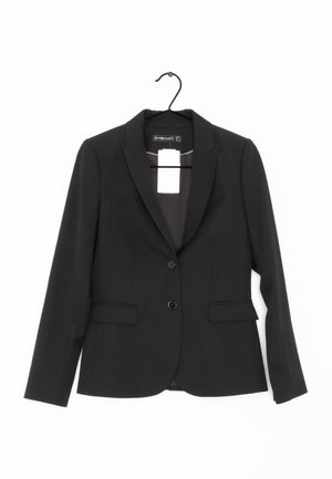 Blazer noir avec une fermeture à un bouton, deux poches avant, des épaules structurées et une texture lisse. Suspendu à un crochet noir.