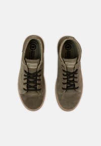 Zöld velúr sneakers, gumitalppal, fekete fűzőkkel és kerek orrmintázattal. Jellemzők: logó és varrás részletek a nyelvén és az oldalán.