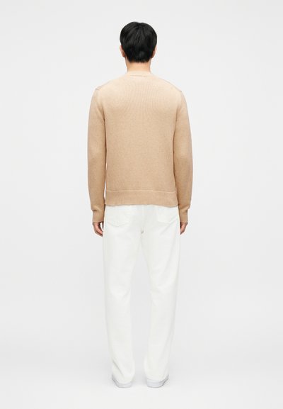 Πουλόβερ από ανοιχτό καφέ πλεκτό ύφασμα με ριμπ μανσέτες και τελείωμα, συνδυασμένο με άσπρο, φαρδύ παντελόνι. Λείο ύφασμα, απλός σχεδιασμός, χωρίς ορατά σχέδια.
