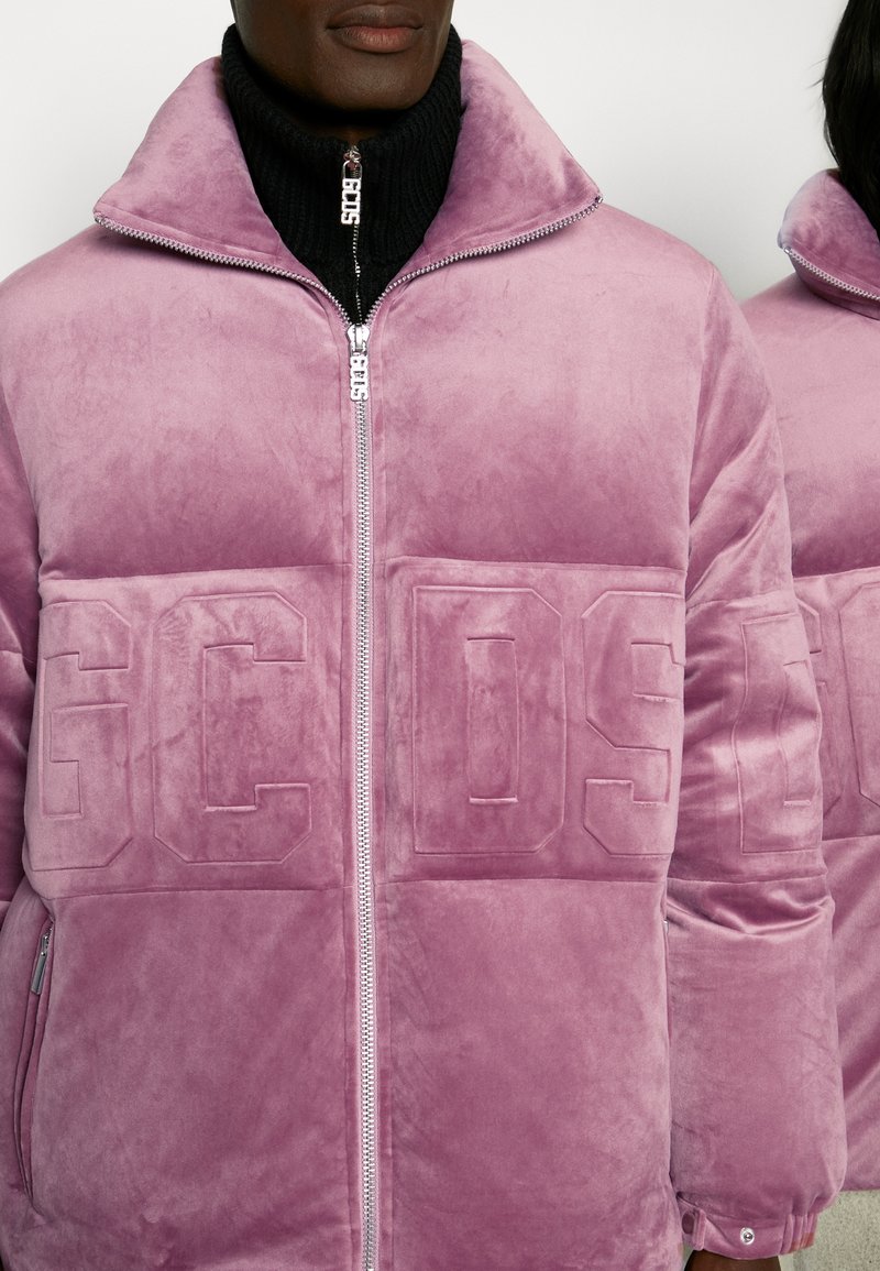 Giacca puffer in velluto rosa con colletto alto, zip frontale e dettaglio del logo in rilievo. Presenta due tasche laterali e una texture liscia e morbida.