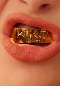 Labios sosteniendo una barra metálica dorada grabada con "KIKO MILANO" en letras en negrita.