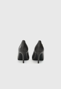 Mustmust musta kõrge kontsaga kingad terava ninaga ja kitsaste stiletto-kontsadega. Sile tekstuur, minimalistlik disain ja kõikide brändi elementide tähelepanu. 