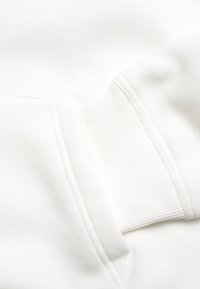 Weißes Sweatshirt mit geripptem Bündchen und aufgesetzter Tasche. Der Stoff hat eine weiche Textur und ein glattes Finish.