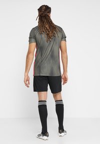 Idrottströja i mörkgrön med vertikala ränder, matchad med svarta shorts. Utrustad med svarta knähöga strumpor med vita ränder och fotbollsskor.