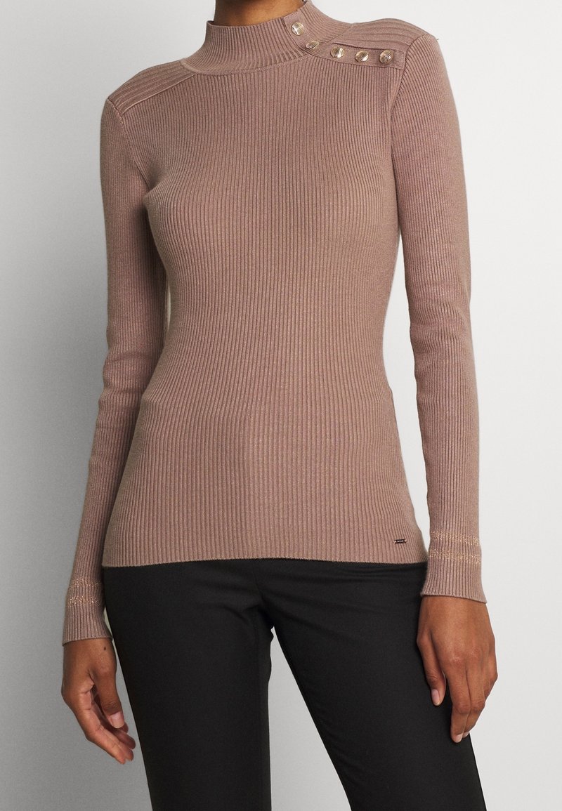 Haut mauve à manches longues en maille côtelée avec col montant et boutons décoratifs sur l'épaule, porté avec un pantalon noir.
