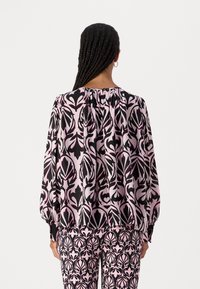 Blouse à manches longues avec un motif floral noir, rose et blanc, présentant un col froncé et une coupe ample. Manches plissées avec des poignets à boutons.