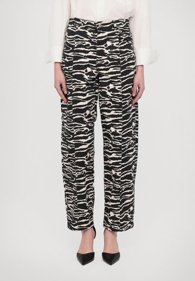 Schwarz-weiße Zebra-Print-Hosen, lockere Passform, mit Vorderfalten und Taschen, kombiniert mit schwarzen spitzen Absatzschuhen.