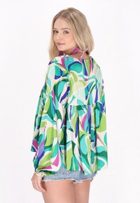Blusa multicolore con un design fluido caratterizzata da motivi astratti in verde, blu e viola. Tessuto leggero con maniche lunghe e vita arricciata.